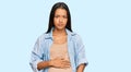 Beautiful hispanic woman expecting a baby showing pregnant belly with serious expression on face Royalty Free Stock Photo