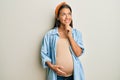 Beautiful hispanic woman expecting a baby, touching pregnant belly with hand on chin thinking about question, pensive expression Royalty Free Stock Photo