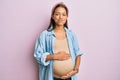 Beautiful hispanic woman expecting a baby, touching pregnant belly puffing cheeks with funny face Royalty Free Stock Photo