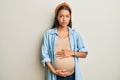 Beautiful hispanic woman expecting a baby, touching pregnant belly relaxed with serious expression on face Royalty Free Stock Photo