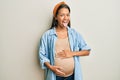 Beautiful hispanic woman expecting a baby, touching pregnant belly sticking tongue out happy with funny expression Royalty Free Stock Photo