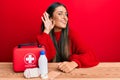 Beautiful hispanic woman with first aid kit smiling with hand over ear listening and hearing to rumor or gossip Royalty Free Stock Photo