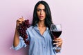 Beautiful hispanic woman holding branch of fresh grapes and red wine clueless and confused expression Royalty Free Stock Photo