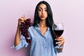 Beautiful hispanic woman holding branch of fresh grapes and red wine puffing cheeks with funny face Royalty Free Stock Photo