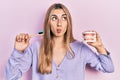 Beautiful hispanic woman holding denture and toothbrush making fish face with mouth and squinting eyes, crazy and comical