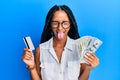 Beautiful hispanic woman holding dollars and credit card sticking tongue out happy with funny expression Royalty Free Stock Photo