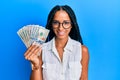 Beautiful hispanic woman holding dollars looking positive and happy standing and smiling with a confident smile showing teeth Royalty Free Stock Photo