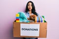 Beautiful hispanic woman holding donation box with toys puffing cheeks with funny face