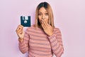 Beautiful hispanic woman holding floppy disk covering mouth with hand, shocked and afraid for mistake Royalty Free Stock Photo