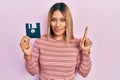 Beautiful hispanic woman holding floppy disk smiling with an idea or question pointing finger with happy face, number one Royalty Free Stock Photo