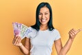 Beautiful hispanic woman holding indian rupee banknotes pointing thumb up to the side smiling happy with open mouth Royalty Free Stock Photo