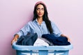 Beautiful hispanic woman holding laundry basket smiling looking to the side and staring away thinking