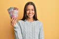 Beautiful hispanic woman holding 100 new zealand dollars banknote looking positive and happy standing and smiling with a confident Royalty Free Stock Photo