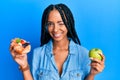 Beautiful hispanic woman holding pastry and healthy green apple winking looking at the camera with sexy expression, cheerful and Royalty Free Stock Photo