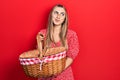 Beautiful hispanic woman holding picnic wicker basket smiling looking to the side and staring away thinking