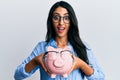 Beautiful hispanic woman holding piggy bank with glasses celebrating crazy and amazed for success with open eyes screaming excited Royalty Free Stock Photo