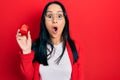 Beautiful hispanic woman with nose piercing holding engagement ring for proposal scared and amazed with open mouth for surprise, Royalty Free Stock Photo