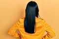 Beautiful hispanic woman with nose piercing wearing yellow leather jacket standing backwards looking away with arms on body