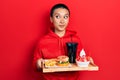 Beautiful hispanic woman with short hair eating a tasty classic burger with fries and soda smiling looking to the side and staring Royalty Free Stock Photo