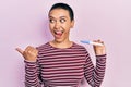 Beautiful hispanic woman with short hair holding pregnancy test result pointing thumb up to the side smiling happy with open mouth Royalty Free Stock Photo