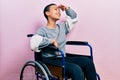 Beautiful hispanic woman with short hair sitting on wheelchair very happy and smiling looking far away with hand over head Royalty Free Stock Photo