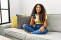 Beautiful hispanic woman sitting on the sofa at home using smartphone with a happy and cool smile on face Royalty Free Stock Photo