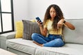 Beautiful hispanic woman sitting on the sofa at home using smartphone pointing down looking sad and upset, indicating direction Royalty Free Stock Photo