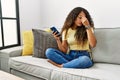 Beautiful hispanic woman sitting on the sofa at home using smartphone tired rubbing nose and eyes feeling fatigue and headache Royalty Free Stock Photo