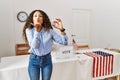 Beautiful hispanic woman standing by at political campaign by voting ballot looking at the camera blowing a kiss with hand on air