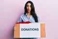 Beautiful hispanic woman volunteer holding donations box in shock face, looking skeptical and sarcastic, surprised with open mouth Royalty Free Stock Photo