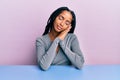 Beautiful hispanic woman wearing casual clothes sitting on the table sleeping tired dreaming and posing with hands together while Royalty Free Stock Photo