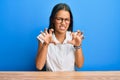 Beautiful hispanic woman wearing casual clothes sitting on the table smiling funny doing claw gesture as cat, aggressive and sexy Royalty Free Stock Photo