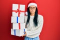 Beautiful hispanic woman wearing christmas hat and holding gifts skeptic and nervous, frowning upset because of problem