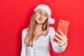 Beautiful hispanic woman wearing christmas hat using smartphone looking at the camera blowing a kiss being lovely and sexy Royalty Free Stock Photo