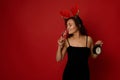 Beautiful Hispanic woman wearing a deer antler hoop and black velvet dress holding an alarm clock and drinking sparkling wine from