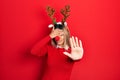 Beautiful hispanic woman wearing deer christmas hat and red nose covering eyes with hands and doing stop gesture with sad and fear Royalty Free Stock Photo