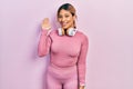 Beautiful hispanic woman wearing gym clothes and using headphones waiving saying hello happy and smiling, friendly welcome gesture Royalty Free Stock Photo