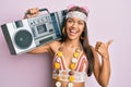 Beautiful hispanic woman wearing hippie style holding boom box pointing thumb up to the side smiling happy with open mouth Royalty Free Stock Photo