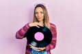 Beautiful hispanic woman wearing hippie style holding vinyl disc relaxed with serious expression on face