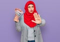 Beautiful hispanic woman wearing islamic hijab holding australian dollars banknotes with open hand doing stop sign with serious Royalty Free Stock Photo