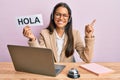 Beautiful hispanic woman wearing operator headset holding hola greenting smiling happy pointing with hand and finger to the side