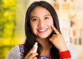 Beautiful hispanic woman wearing white blouse with colorful embroidery, applying cream onto face using finger during Royalty Free Stock Photo