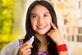 Beautiful hispanic woman wearing white blouse with colorful embroidery, applying cream onto face using finger during Royalty Free Stock Photo