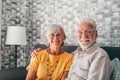 Beautiful hoary good-looking mature spouses relaxing together on comfy couch at modern home smiling staring at camera feel Royalty Free Stock Photo