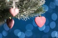 Beautiful holiday heart shaped bauble hanging on Christmas tree against blue background with blurred festive lights Royalty Free Stock Photo