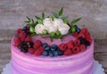 Beautiful home cake with pink and purple cream, decorated with white roses and berries of BlackBerry, blueberries, raspberries Royalty Free Stock Photo