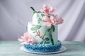 A beautiful home wedding three-tiered cake decorated with pink flowers and branches with green leaves in a rustic style. Royalty Free Stock Photo