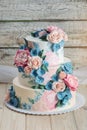 A beautiful home wedding three-tiered cake decorated with pink roses and blue flowers in a rustic style on wooden table Royalty Free Stock Photo