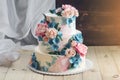 A beautiful home wedding three-tiered cake decorated with pink roses and blue flowers in a rustic style on wooden table Royalty Free Stock Photo