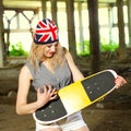 Beautiful hot summer girl in shorts and a hat with a picture of the British flag holding skateboard.A beautiful hot summer young g